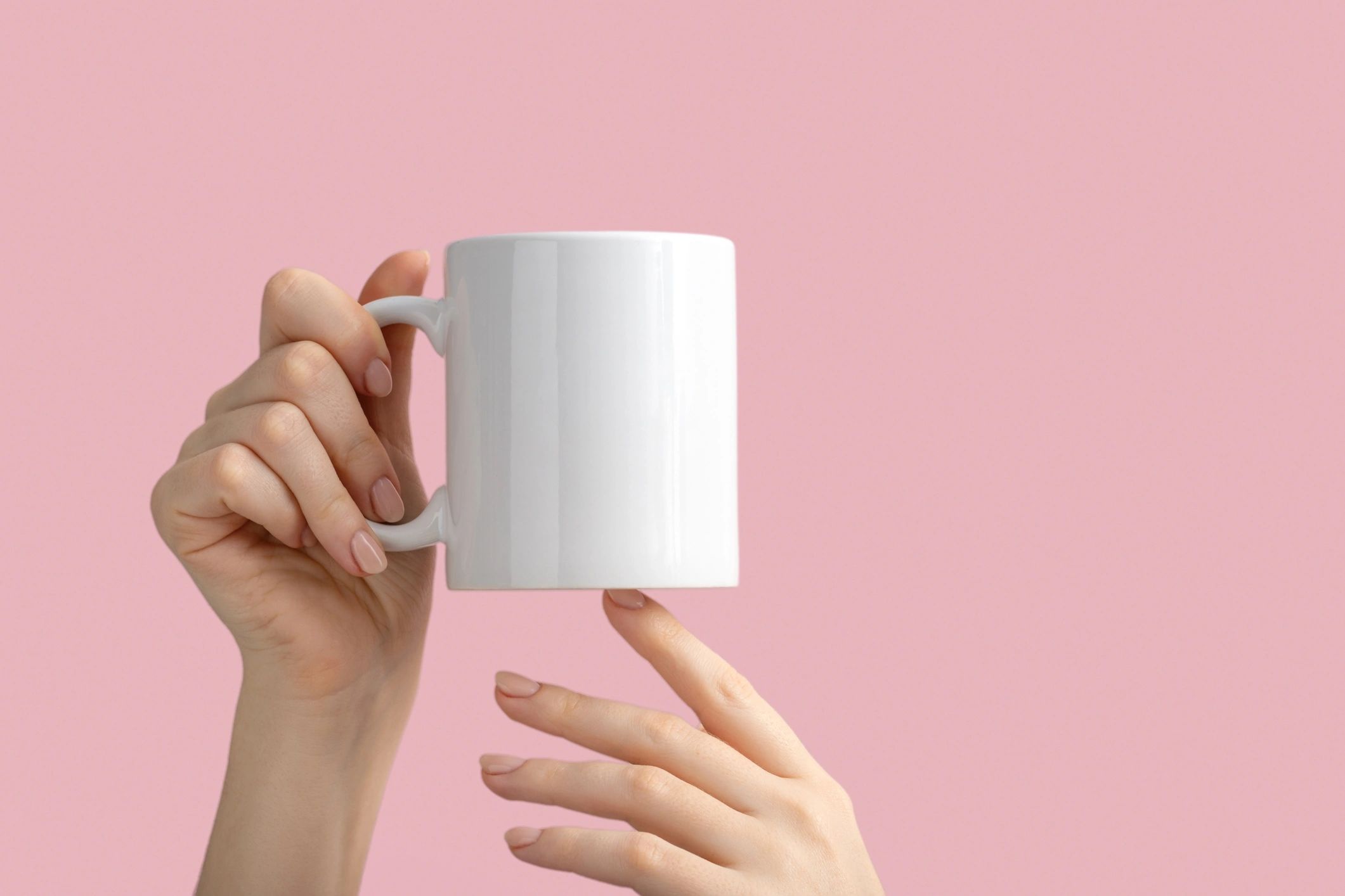 Hands holding a blank mug on a pink background