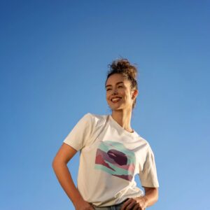 Lifestyle mockup of a unisex t-shirt on a model in a minimal setting with warm neutral tones and copy space for a simple artistic graphic (soft pink/blue accents).