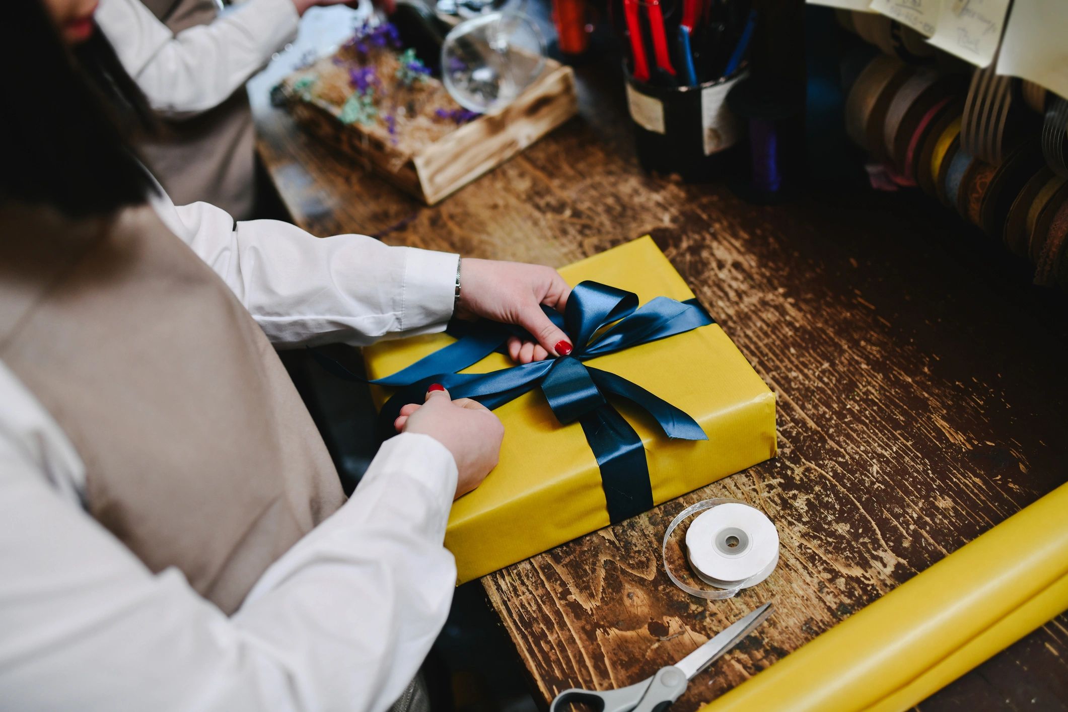 Hands tying a blue ribbon bow on a gift box